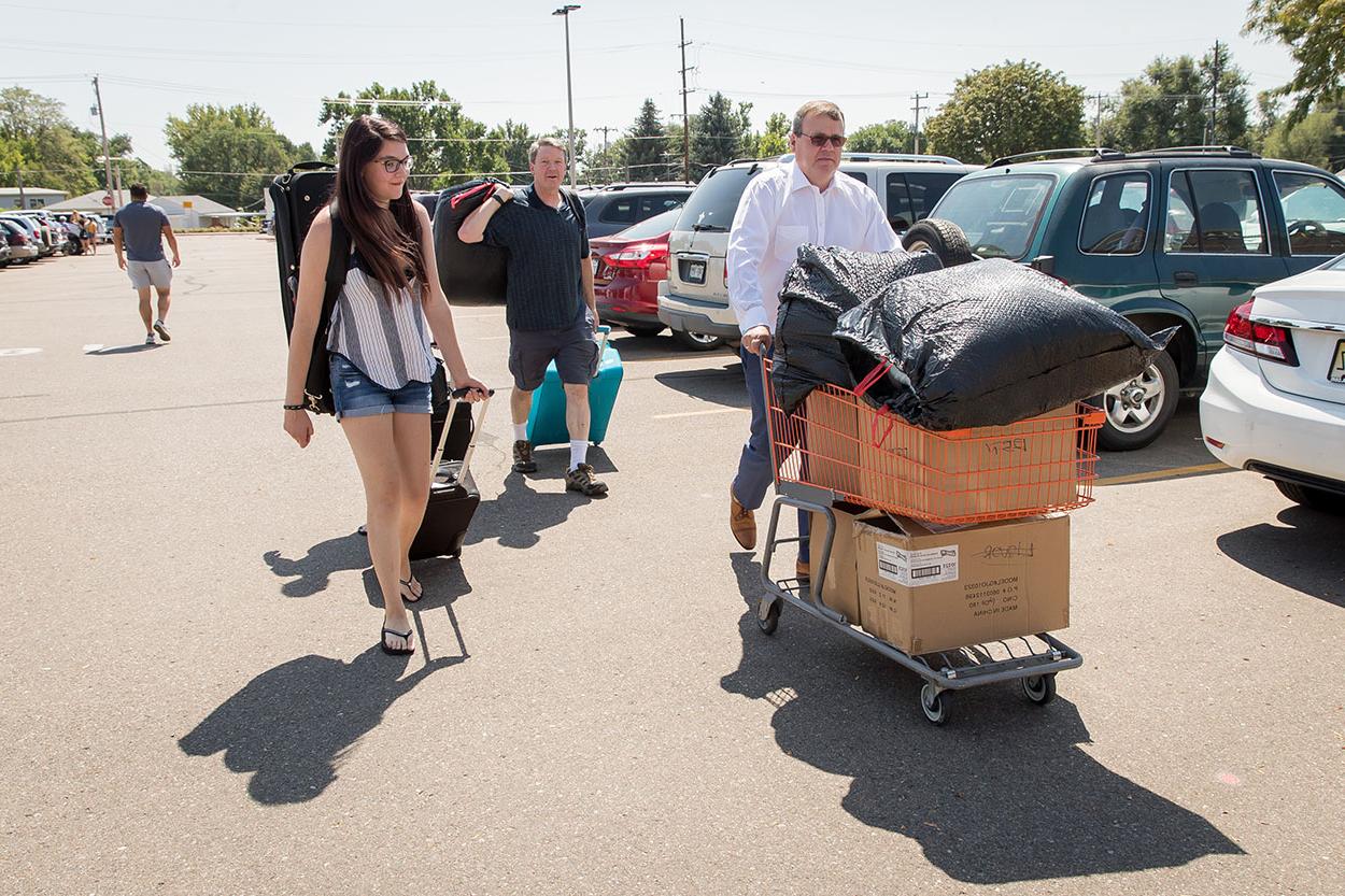 President Feinstein rolls a cart full of student's luggage alongside students moving into campus.